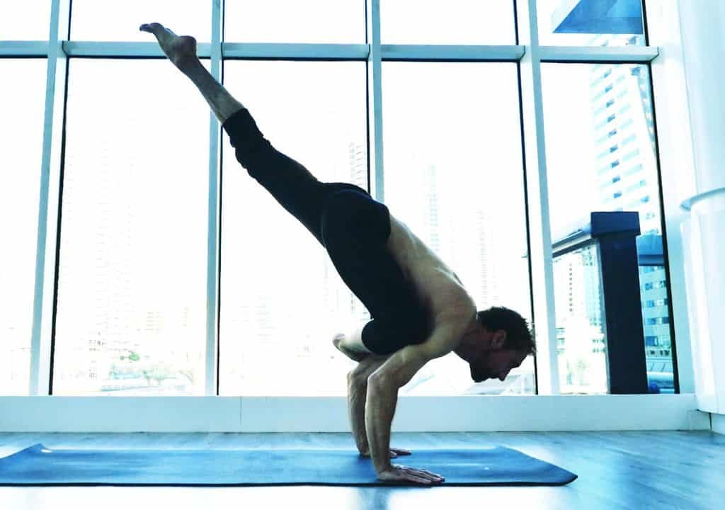 Hombre practicando yoga en postura de equilibrio en un estudio luminoso.
