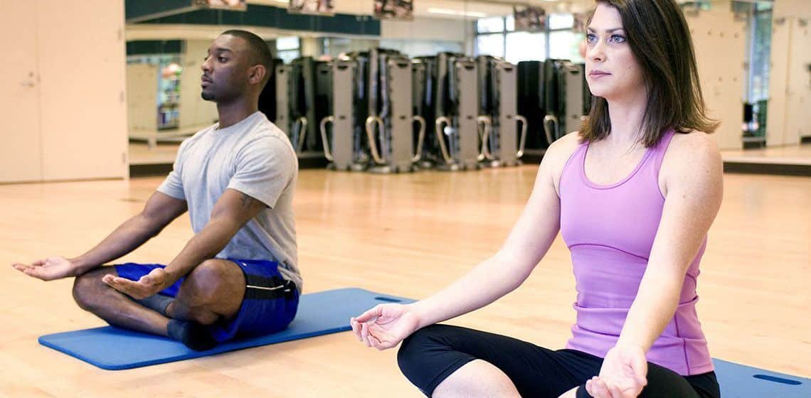 Persona practicando yoga en gimnasio, enfoque en bienestar y salud.